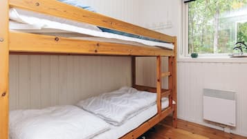 Et soveværelse med køjesenge, hvidt sengetøj, et vindue med udsigt til træer og en radiator.