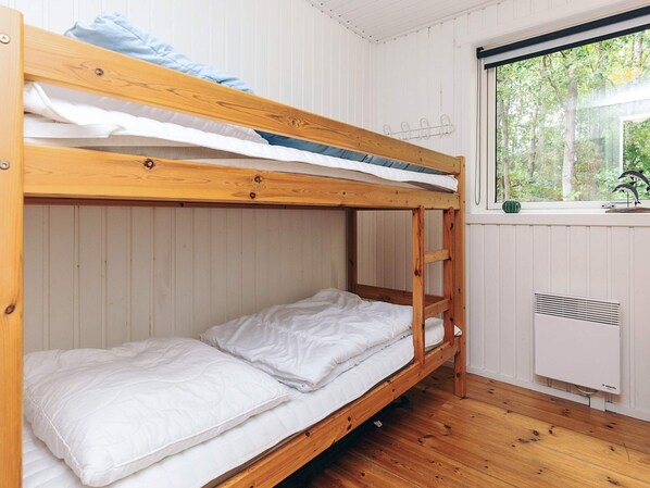A bunk bed room with white bedding, a window with a view of trees, and a radiator.