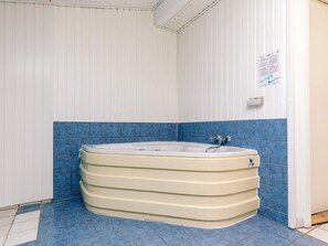 Una bañera de esquina con tina blanca y azulejos azules en el suelo y las paredes.