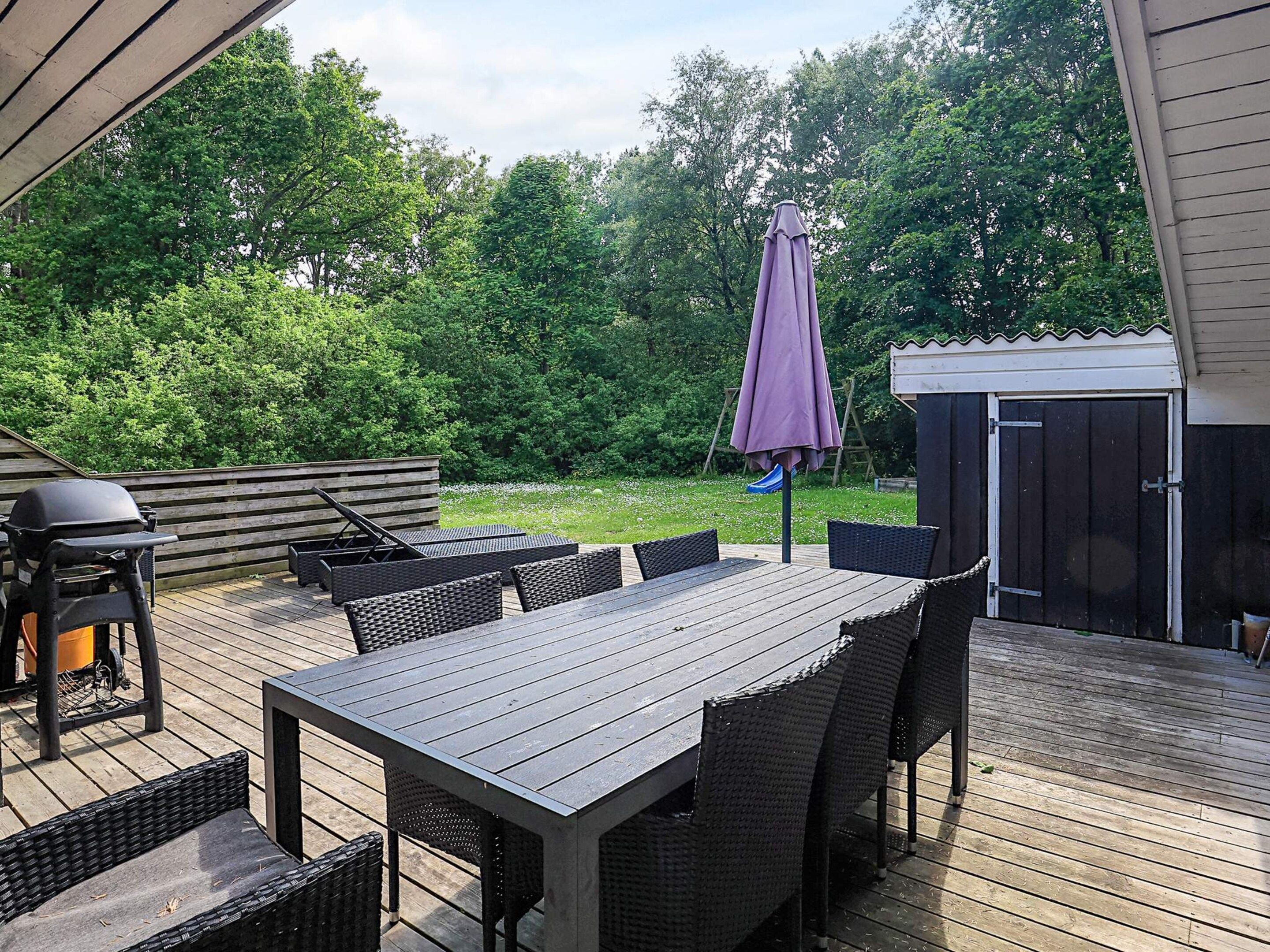 En udendørs terrasse med et træbord og stole, grill og et overdækket parasol.