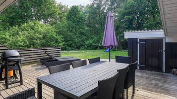 En udendørs terrasse med et træbord og stole, grill og et overdækket parasol.