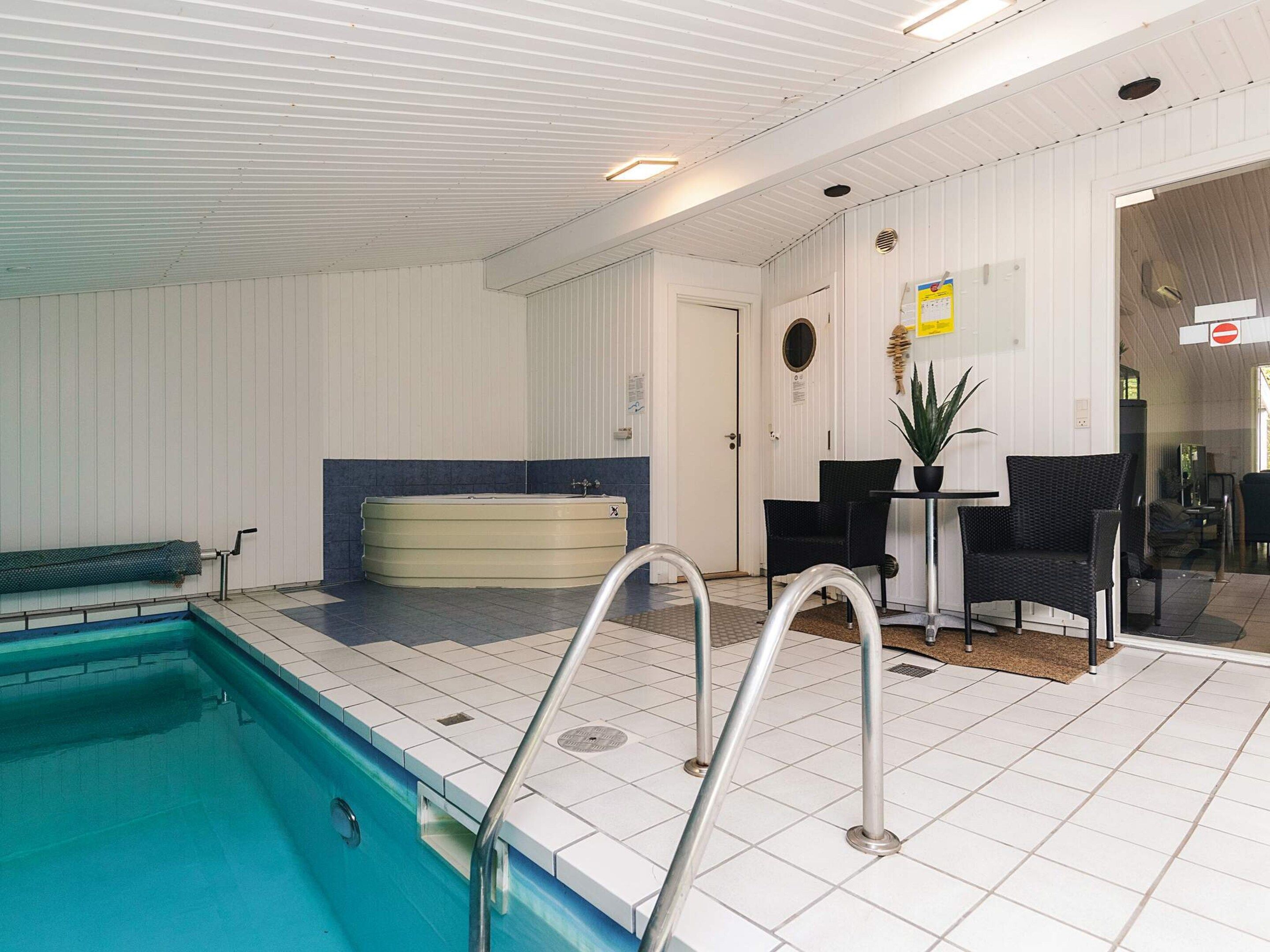 En swimmingpool med en nedsænket bænk, et spabad og et opholdsområde med stole og et bord.