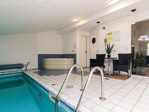 En swimmingpool med en nedsænket bænk, et spabad og et opholdsområde med stole og et bord.
