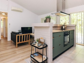 Una cocina moderna con horno empotrado, un área de comedor con sofá y televisor, y un carrito pequeño con cuencos.