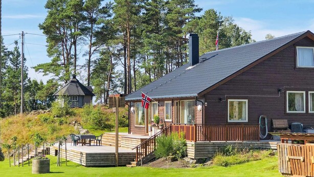 A wooden cabin with a deck, surrounded by trees and a flag. - 8 Person Holiday Home in Jelsa (Suldal)