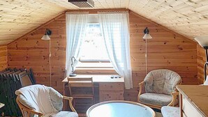 A cozy attic room with wooden walls, a small desk, two chairs, a round table, and a window with curtains. - 8 Person Holiday Home in Jelsa (Suldal)