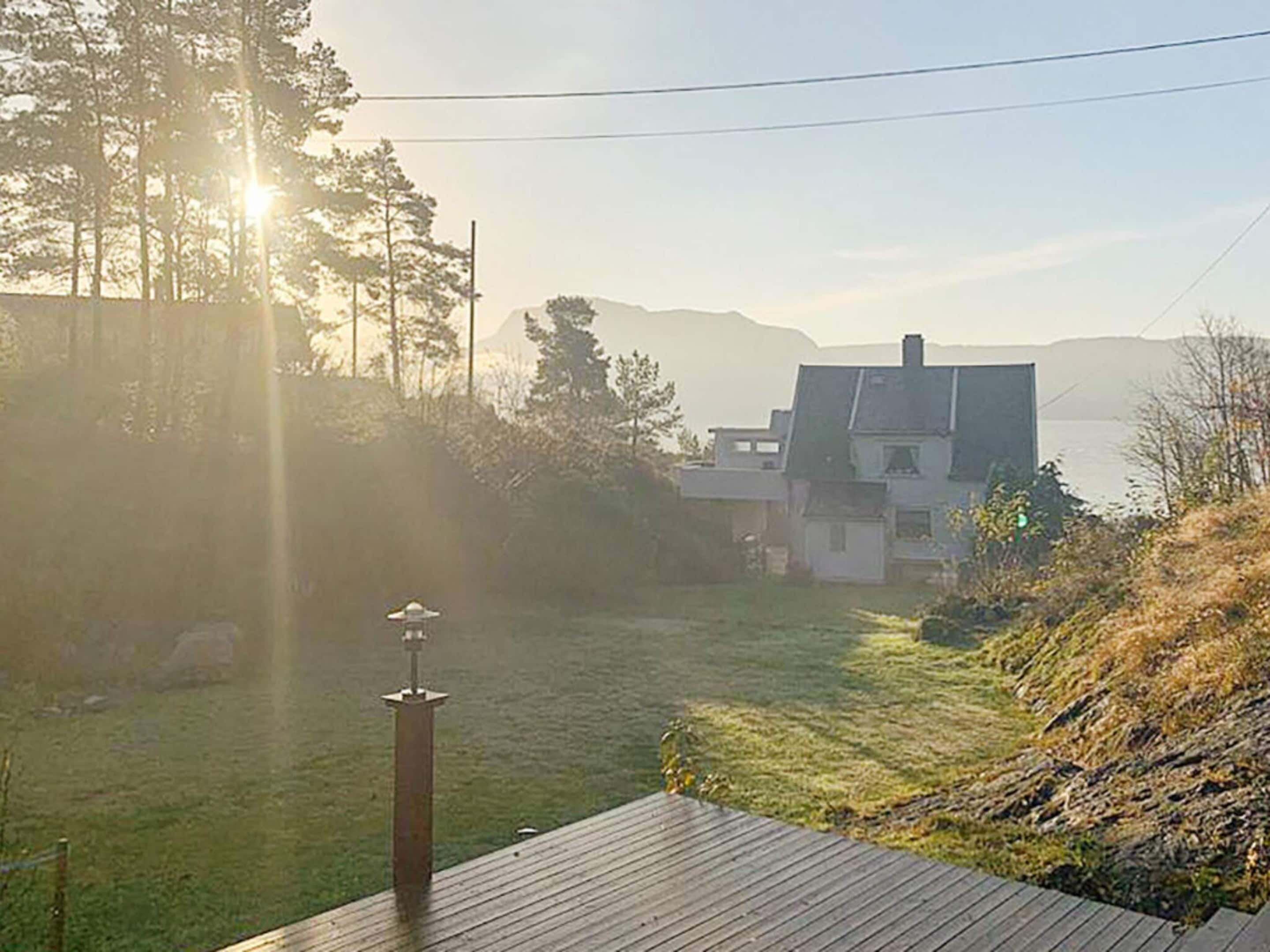 Una terraza de madera con vistas a un área verde, una casa y montañas al fondo.