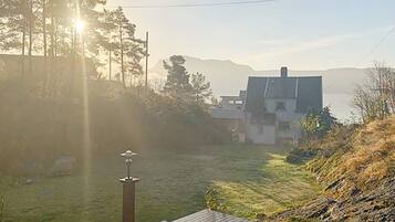 Una terraza de madera con vistas a un área verde, una casa y montañas al fondo.