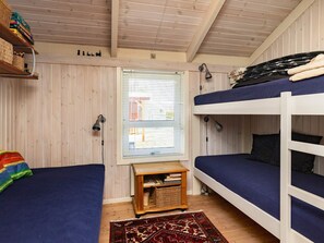 Una habitación con dos literas, una pequeña mesa de madera con libros, una ventana con persianas y una alfombra estampada.