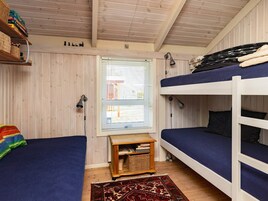 Una habitación con dos literas, una pequeña mesa de madera con libros, una ventana con persianas y una alfombra estampada.