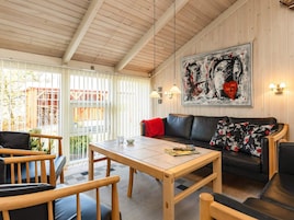 Una habitación acogedora con techo de madera, un sofá de cuero negro con cojines estampados, una mesa de madera y un cuadro abstracto grande en la pared.