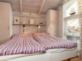 A bedroom with a bed, wooden ceiling, wall-mounted shelves, and a window with blinds.