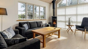 A modern living room with a sofa, armchair, and a wooden coffee table. A fireplace is visible in the background. - 8 Person Holiday Home in Hals (Hals)