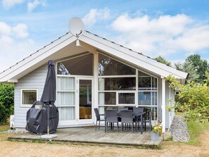 Une maison de plain-pied dotée d’un porche couvert, d’une antenne parabolique et d’une terrasse aménagée avec du mobilier d’extérieur.
