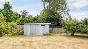A small, single-story shed with a sloped roof, surrounded by a wooden fence and trees.