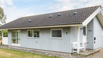 A single-story building with a grey exterior, a tiled roof, and a small porch with a bench.