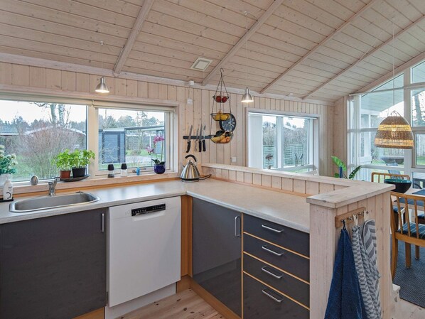 A modern kitchen with wooden cabinets, a dishwasher, and a large window providing a view of the outdoors. - 4 Star Holiday Home in Vaeggerlose (Vaeggerlose)