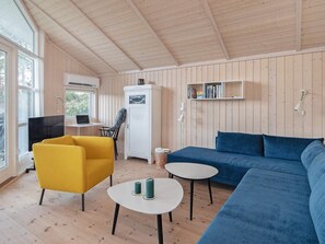 A room with a sofa, a yellow chair, a small table, a bookshelf, and a television. - 4 Star Holiday Home in Vaeggerlose (Vaeggerlose)