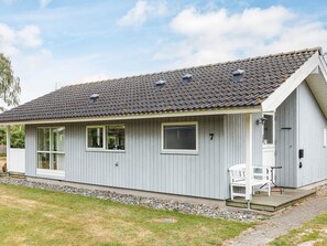 A single-story building with a grey exterior, a tiled roof, and a small porch with a bench. - 4 Star Holiday Home in Vaeggerlose (Vaeggerlose)