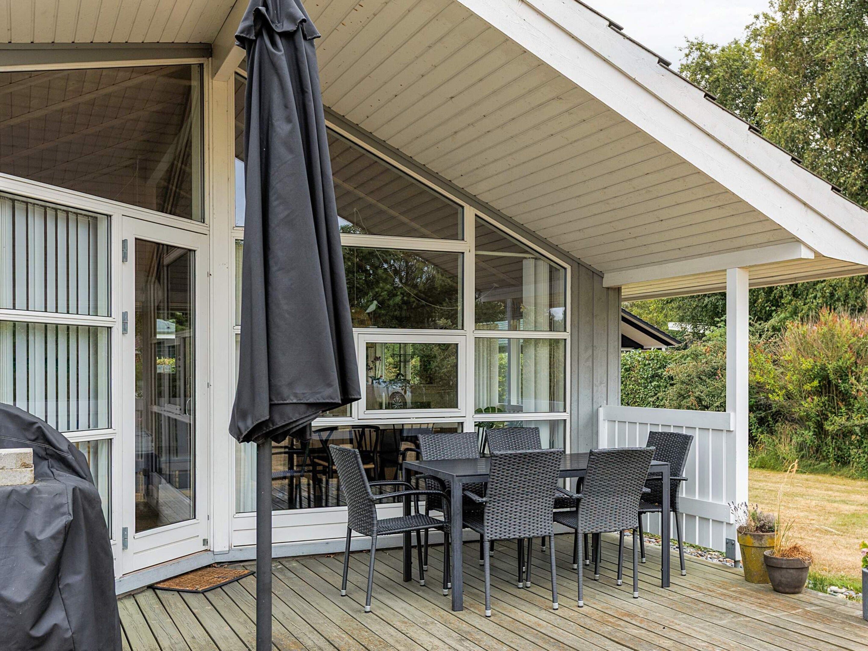 Een overdekt terras met een tafel, stoelen, een schuifpui en een parasol.
