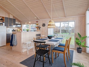 A modern kitchen with wooden cabinets, a dining area with a table and chairs, and a large window offering a view of the outdoors.