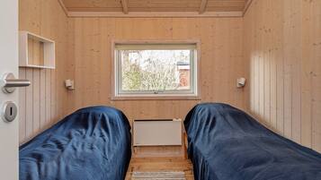 A room with wooden walls, a window, two beds with blue covers, a white shelf, and a door with a keyhole.