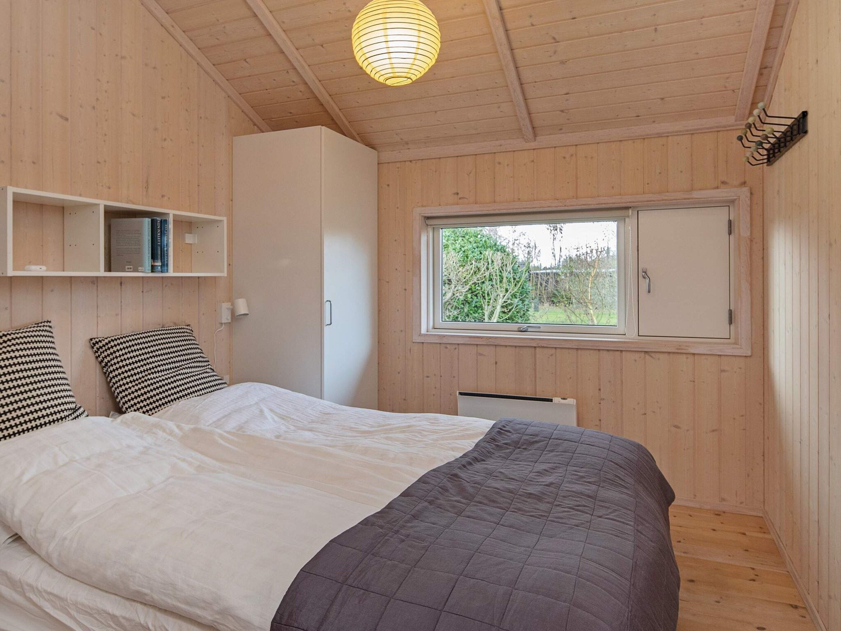 A bedroom with a bed, a window, a wardrobe, and a shelf with books.