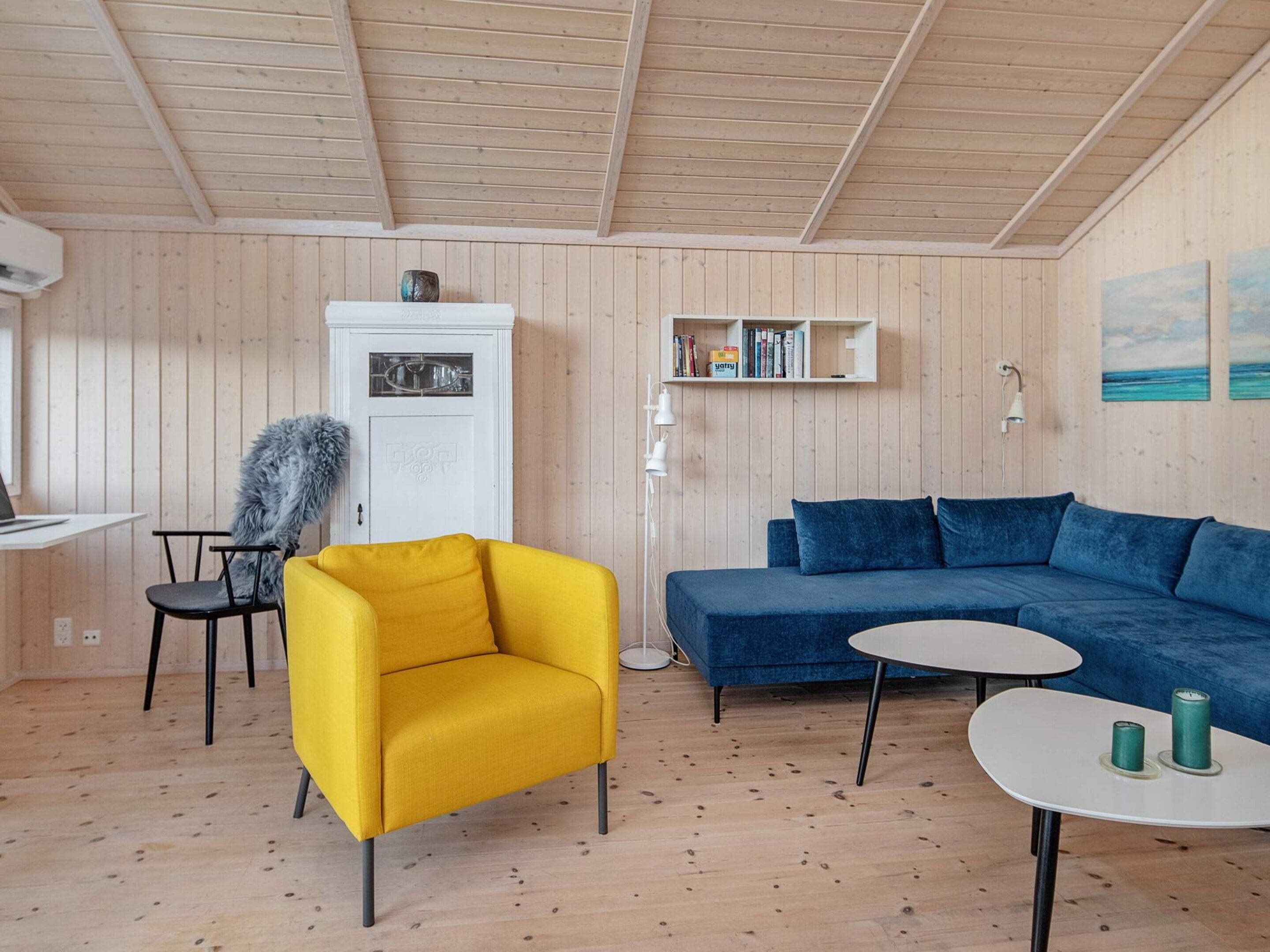 Une pièce avec un fauteuil jaune, un canapé bleu, une armoire blanche et une petite table avec des bougies.