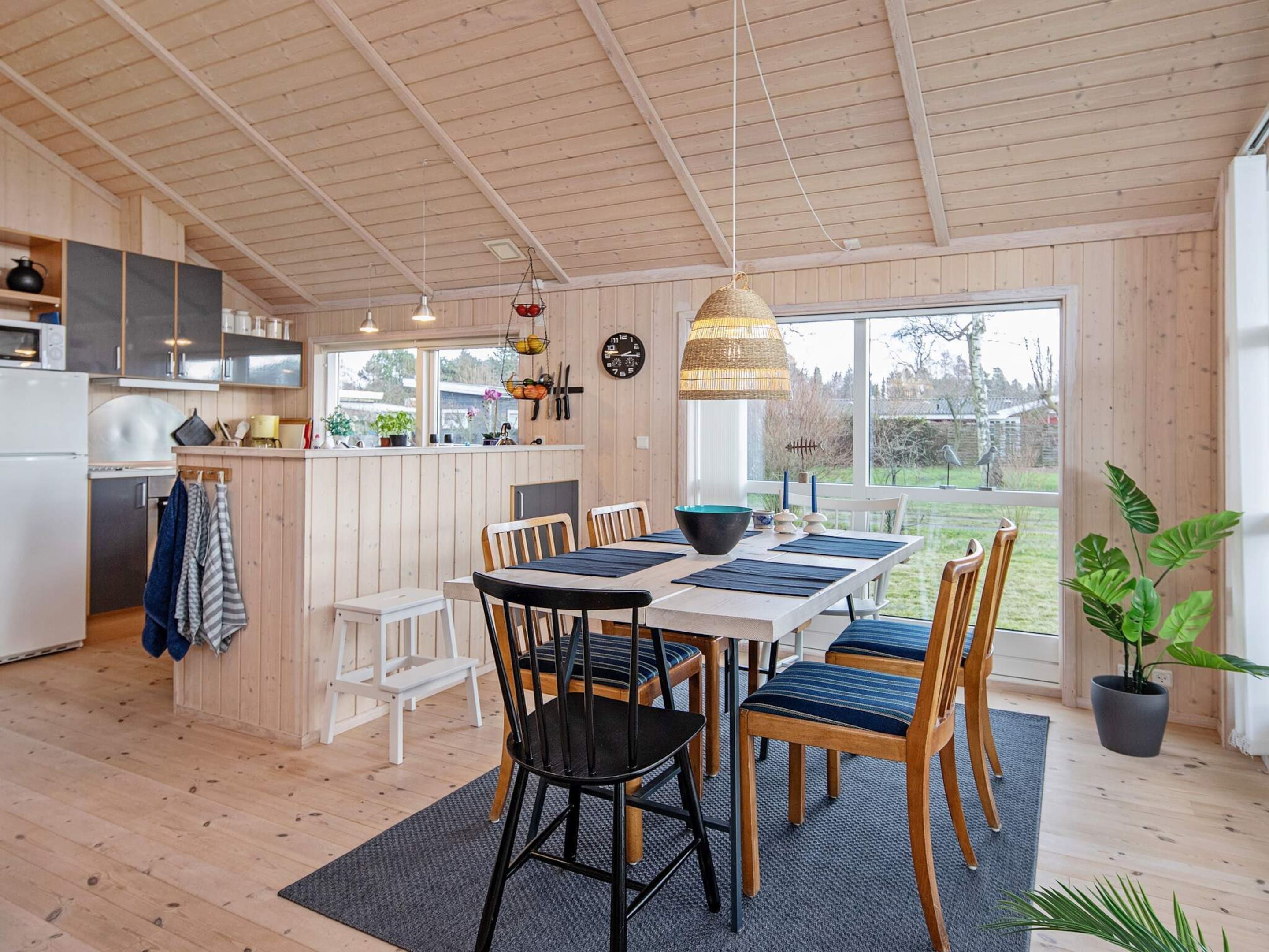 A modern kitchen with wooden cabinets, a dining area with a table and chairs, and a large window offering a view of the outdoors.