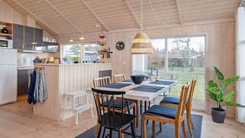 A modern kitchen with wooden cabinets, a dining area with a table and chairs, and a large window offering a view of the outdoors.