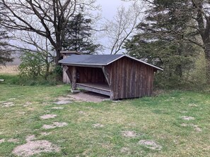 A wooden shed with a sloped roof, situated on a grassy area with trees in the background. - 6 Person Holiday Home in Hovborg (Hovborg)