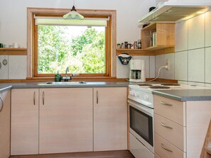 A kitchen with wooden cabinets, a built-in oven, a coffee maker, and a window with a view of greenery. - 6 Person Holiday Home in Hovborg (Hovborg)