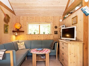A cozy cabin interior with a sofa, a small table, a television, and wooden walls.