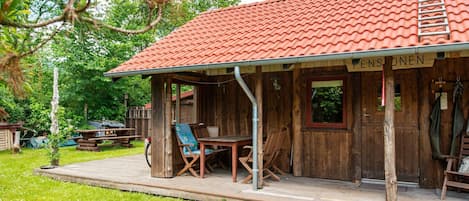 A rustic wooden building with a red-tiled roof, a porch with seating, and a sign that reads 'Pensionen'.
