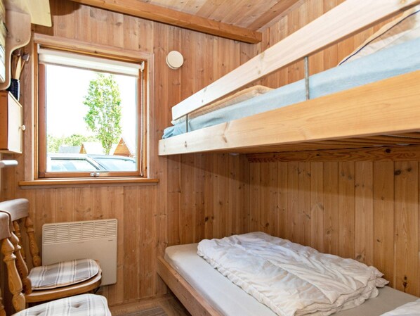 A wooden bunk bed room with a window, a radiator, and a plaid chair.