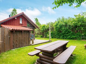 A wooden cabin with a red roof, a picnic table, and a bicycle in the background.