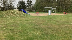 A playground with a blue slide, swings, and a red horse-shaped swing set. - 6 Person Holiday Home in Hovborg (Hovborg)