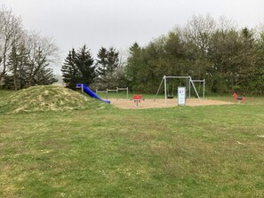 A playground with a blue slide, swings, and a red horse-shaped swing set. - 6 Person Holiday Home in Hovborg (Hovborg)