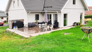 Una casa de dos pisos con un patio cubierto, una parrilla y mobiliario exterior.