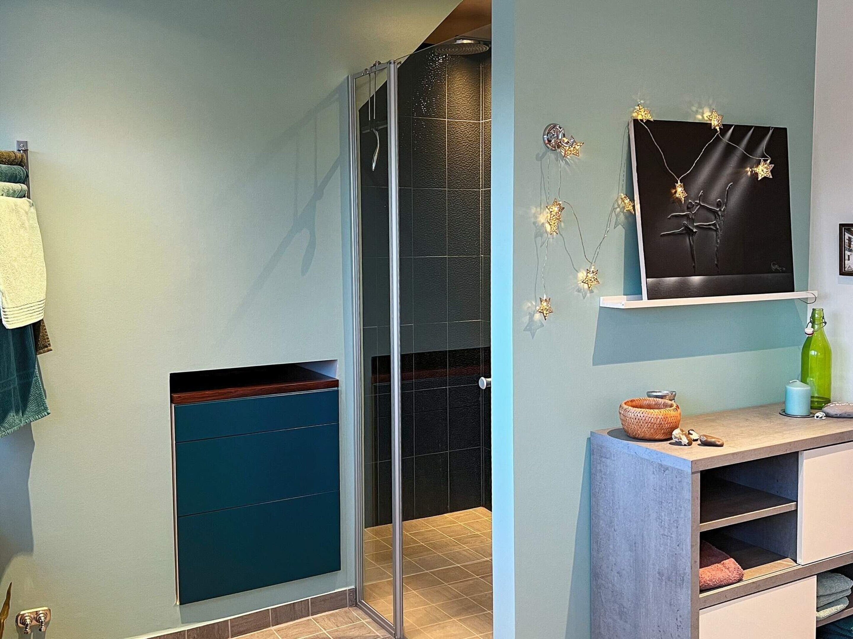 A bathroom with a glass shower enclosure, a towel rack, a sink, and a shelf with decorative items.