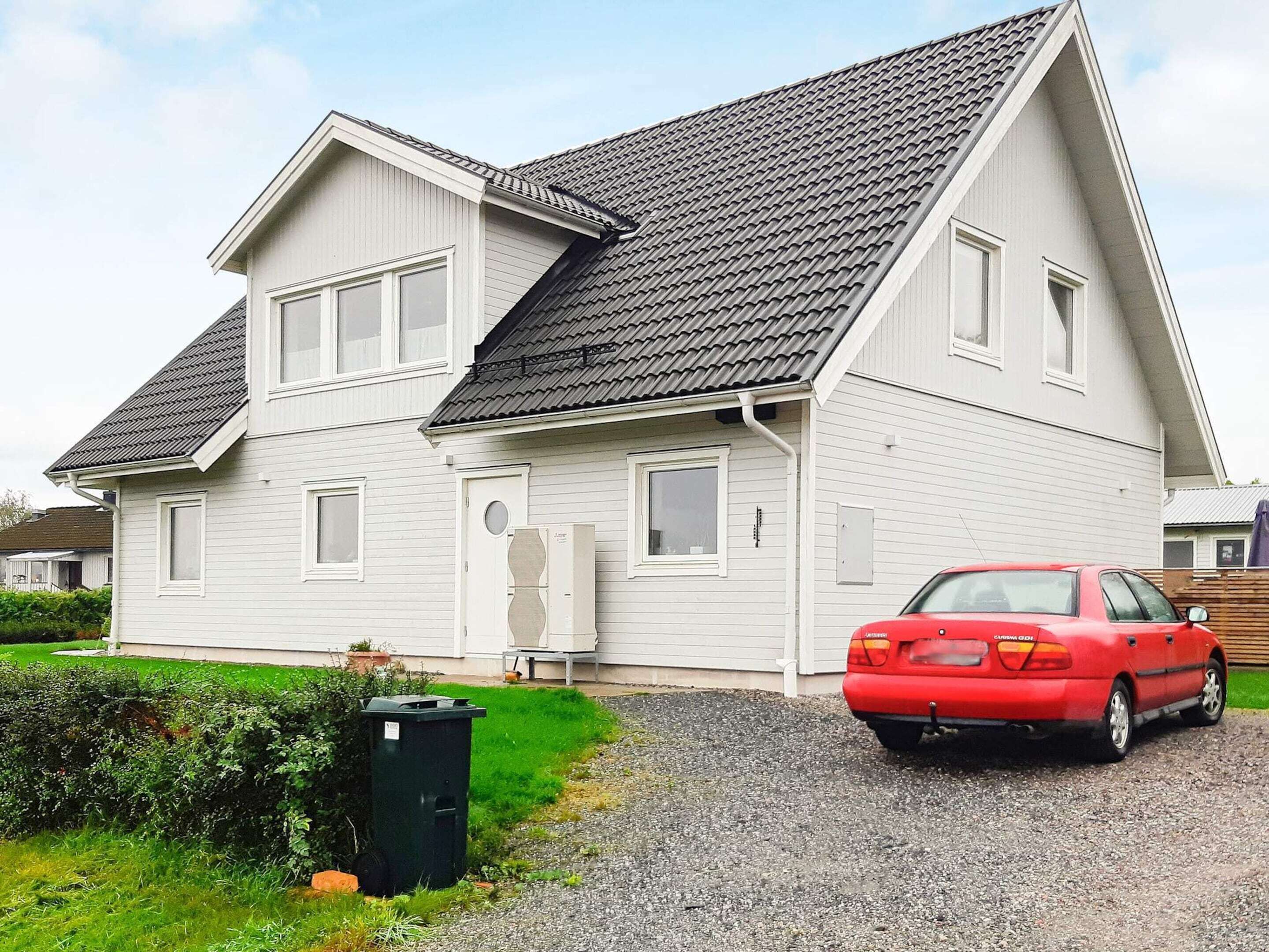 Una casa a due piani con tetto spiovente, un garage anteriore e un'auto rossa parcheggiata nel vialetto.