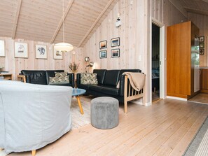 A cozy living room with a black leather sofa, a round coffee table, and a grey ottoman. The room features wooden walls and a high ceiling with exposed beams.