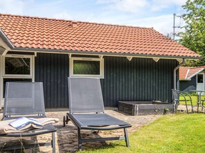 A building with a red-tiled roof, two large windows, and a covered outdoor seating area with two lounge chairs and a table.