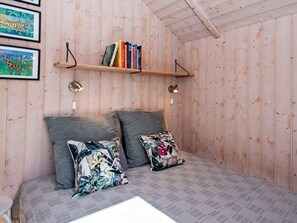 A cozy room with a bed, two pillows, a shelf with books, and framed pictures on the wall.