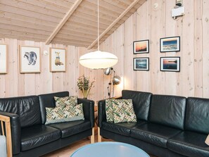 A cozy room with two black leather sofas, a wooden ceiling, and framed pictures on the walls.