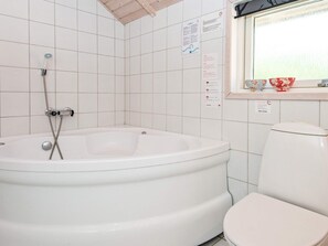 A bathroom with a white bathtub, a toilet, and a window with floral decorations. - 6 Person Holiday Home in Hemmet (Hemmet)