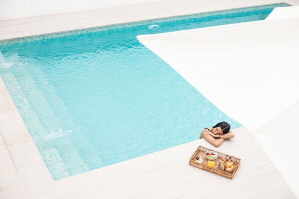 A person relaxing by a poolside with a tray of food and a beverage.