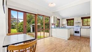 A spacious kitchen with large windows, a dining area with a table and chairs, and wooden flooring. - 12 Bluewater Drive Narooma (Narooma)