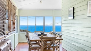 A dining area with a view of the ocean, wooden furniture, and a large window with blinds. - 12 Bluewater Drive Narooma (Narooma)