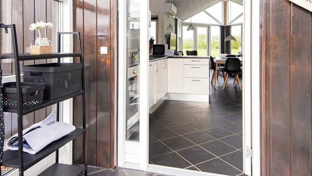 A modern kitchen with white cabinets, a black tiled floor, and a dining area with a table and chairs. - 4 Star Holiday Home in Ansager (Ansager)
